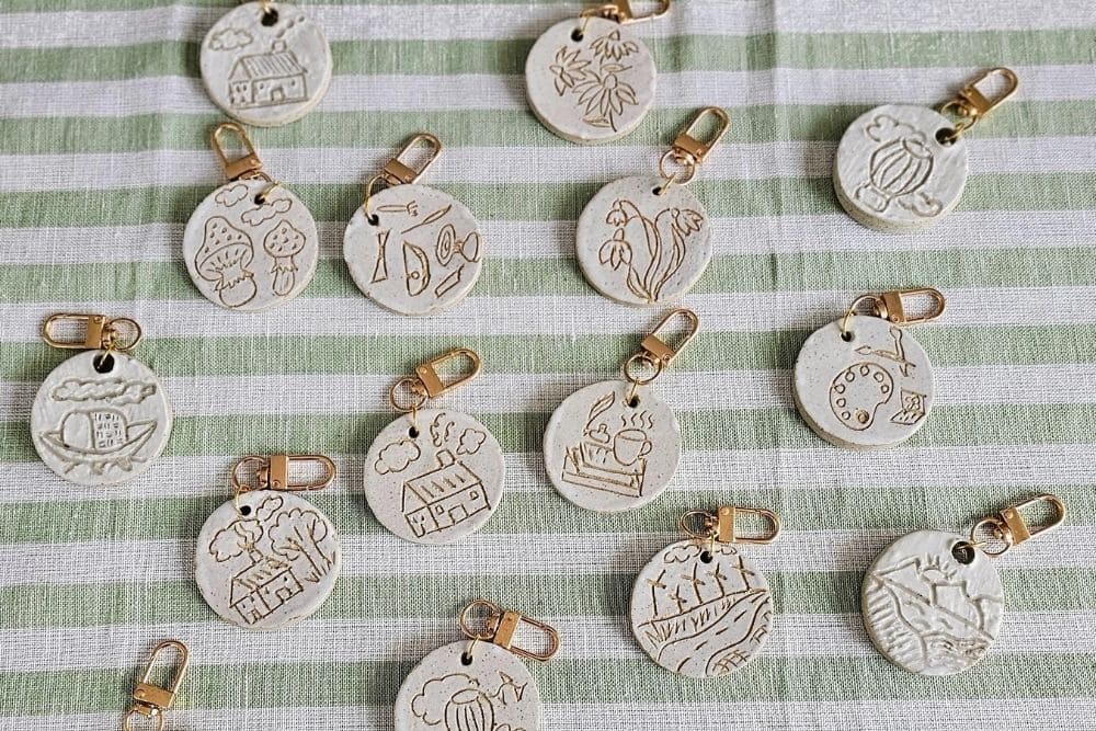 Stamped ceramic keychains with illustrated designs on a green striped fabric